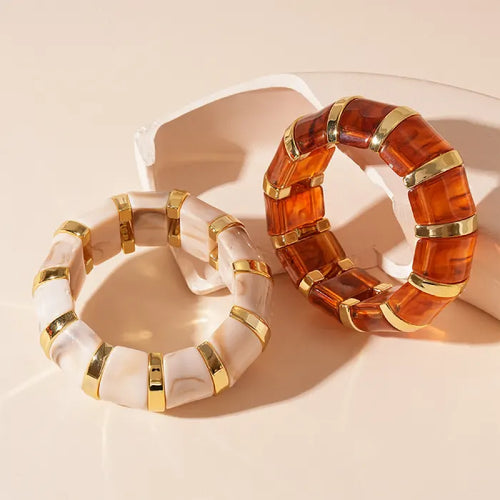 marbled acrylic bracelets in beige and amber tones with gold accents displayed on soft beige surface side by side