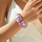 marbled acrylic bracelets in translucent pink with gold accents worn on model’s arm against white outfit