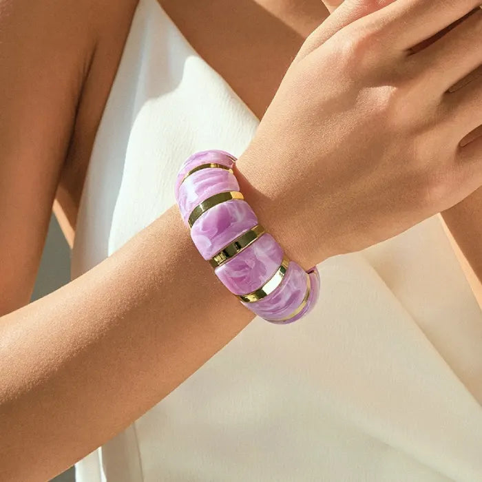 marbled acrylic bracelets in translucent pink with gold accents worn on model’s arm against white outfit