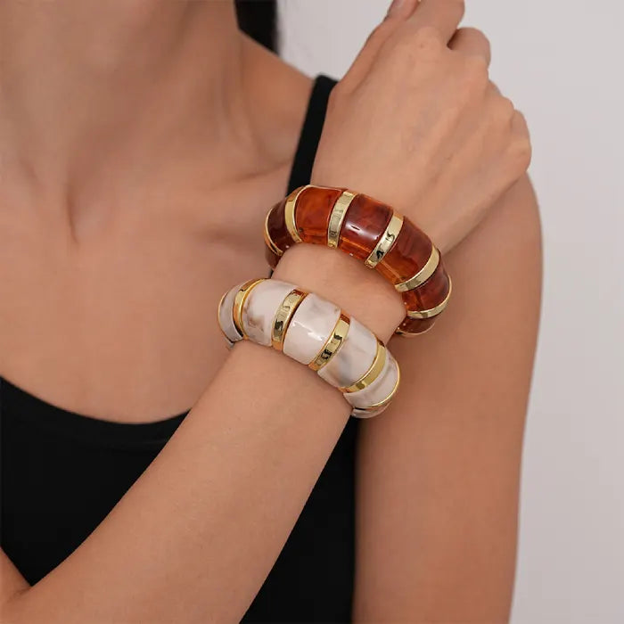 marbled acrylic bracelets in amber and beige tones with gold accents worn stacked on model’s wrist