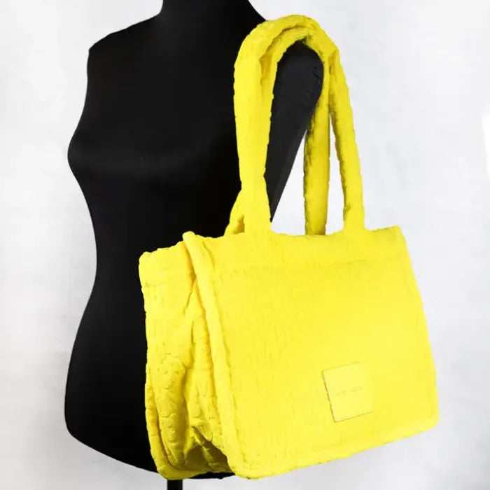 Marc Jacobs Medium Golden Kiwi Monogram Tote Bag in yellow terry fabric on mannequin, featuring embossed logo.