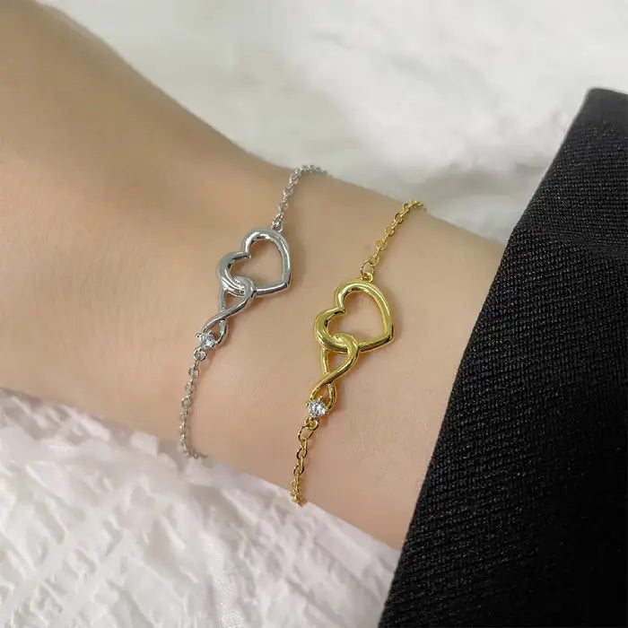 Matching gold and silver heart infinity bracelets with elegant intertwined designs on a wrist.