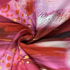 Fabric close-up of maxi dress in pink, orange, and red abstract pattern with silky finish.