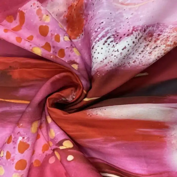 Fabric close-up of maxi dress in pink, orange, and red abstract pattern with silky finish.