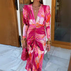  Maxi dress in vivid pink-orange print with ruched detail and plunge neckline styled for an evening event.