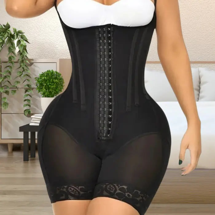 Black waist trainer with hook closure, worn in bedroom setting, featuring sheer mesh and lace detailing.