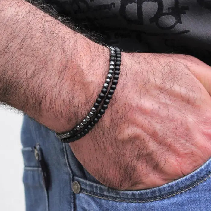 mens bracelet stack.  Close-up of a wrist wearing a black beaded bracelet with a blurred background.