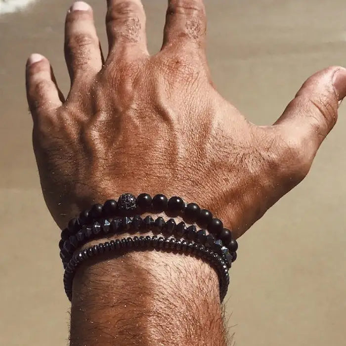 mens bracelet stack. Hand wearing two black beaded bracelets against a neutral background