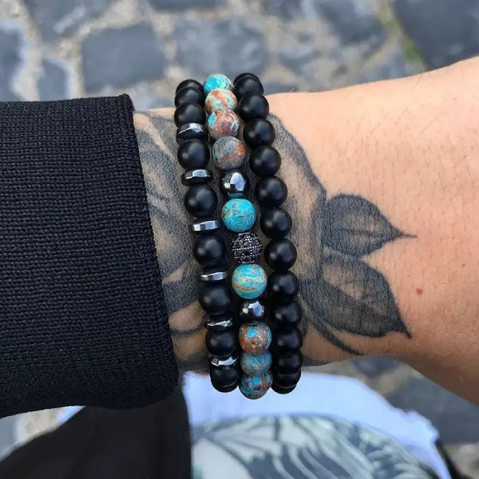 mens bracelet stack. Black beaded bracelet with turquoise stones on a wrist against a blurred background