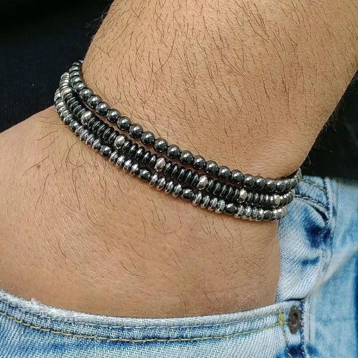 mens bracelet stack.  Close-up of a person's wrist wearing multiple beaded bracelets on a dark background.