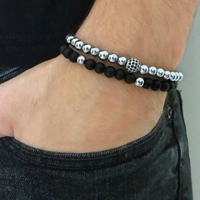 mens bracelet stack. Two beaded bracelets, one black and one silver, on a person's wrist.