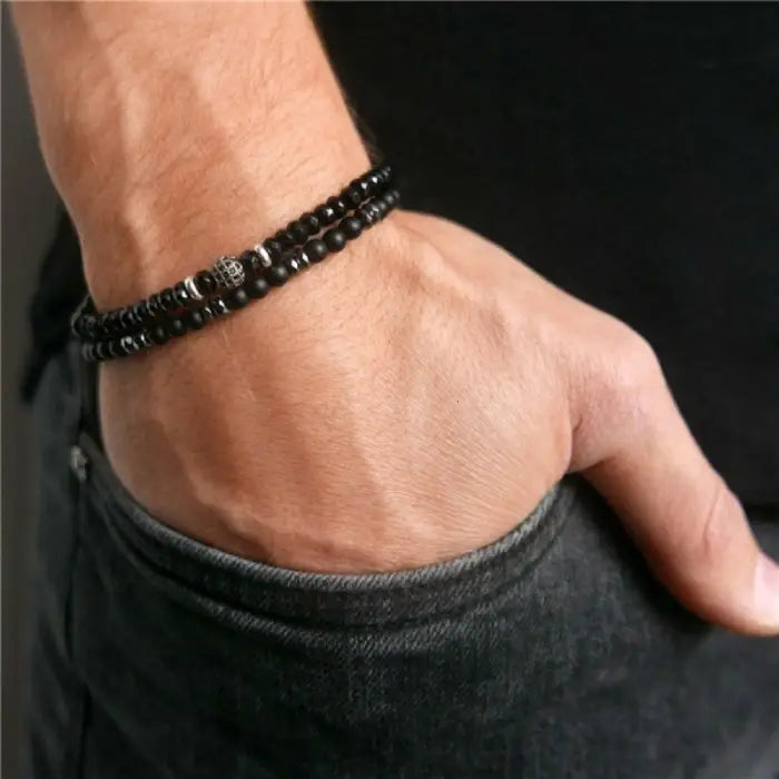mens bracelet stack.  Close-up of a wrist wearing a black beaded bracelet against a dark background