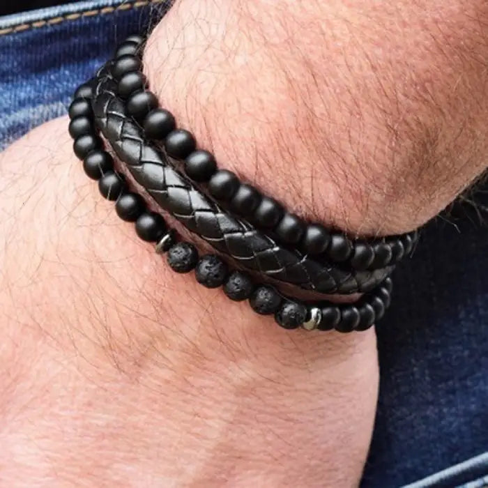 mens bracelet stack. Close-up of a wrist wearing multiple black beaded bracelets on a denim background