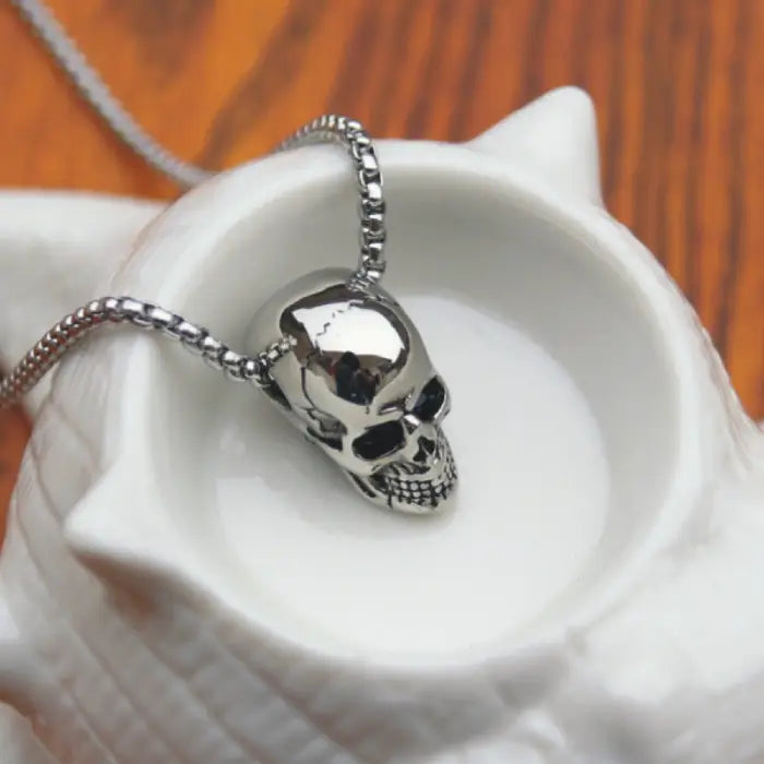 Metallic skull necklace elegantly presented inside a white seashell bowl for a stylish display.