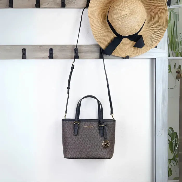 Michael Kors brown monogram tote displayed with straw hat on white wall hooks