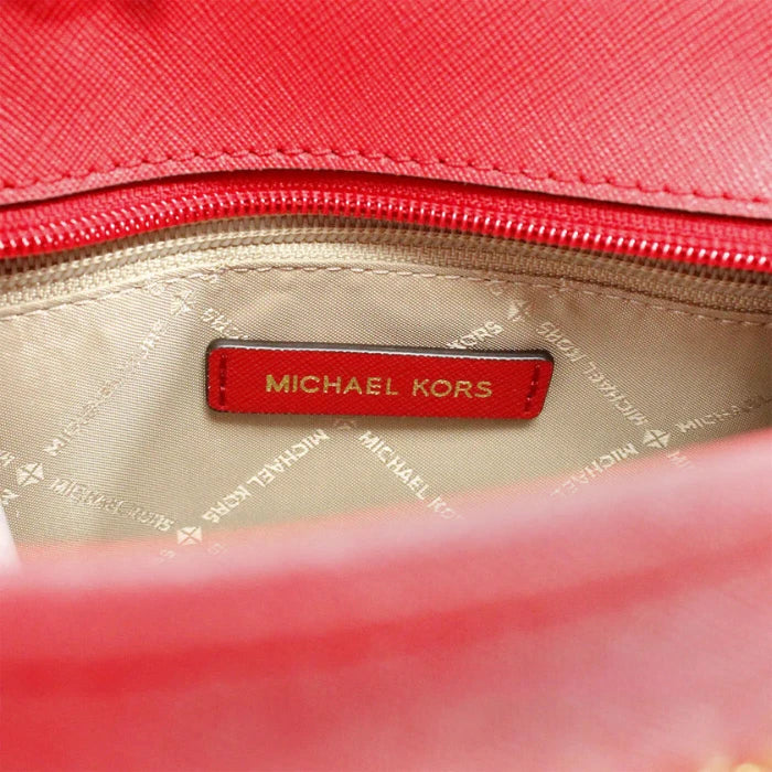 Authentic Michael Kors branded red leather tag inside designer handbag with signature beige monogram fabric lining