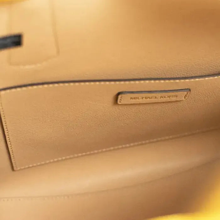 Interior leather label detail of Michael Kors Voyager tote showing brand name on beige lining.