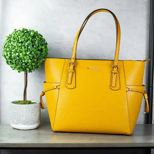 Yellow Michael Kors Voyager tote styled with decorative topiary plant in white geometric planter.