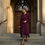 Mid length wool coat in burgundy worn for a formal occasion, featuring a classic cut and timeless feminine elegance.