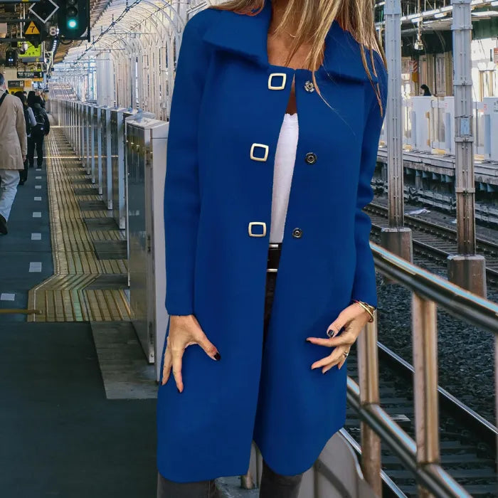 Mid length wool coat in premium blue worn by a woman at a train station, tailored fit with gold buttons for elegant warmth.