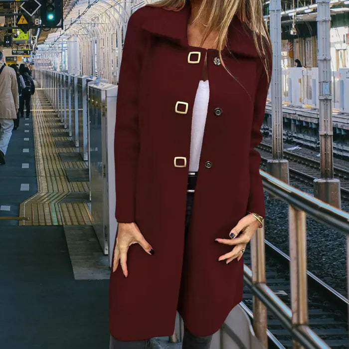 Mid length wool coat in deep burgundy worn by a woman at a train station, tailored silhouette with gold buttons for warmth.