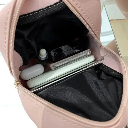 Open pink mini backpack showing interior with personal items including earbuds, smartphone, and cosmetics