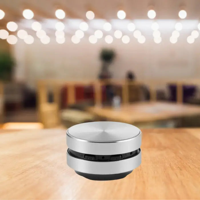 mini bluetooth speaker in silver finish on wooden table with bokeh lighting effect and modern interior background