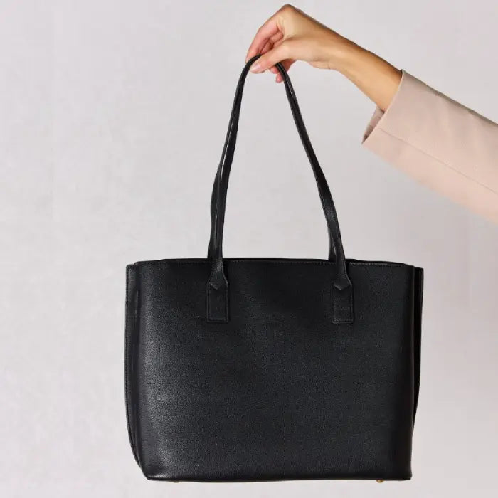 Side view of a sleek black leather tote bag held by a hand, emphasizing its clean lines and spacious interior