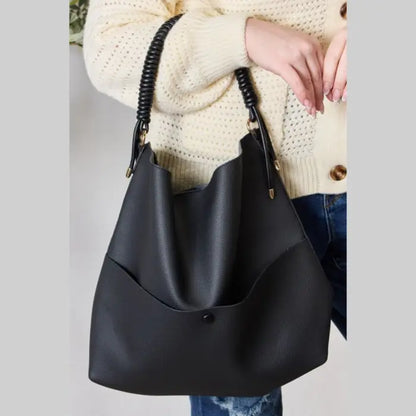 Modern black handbag with coiled handle held by woman in cream knit sweater