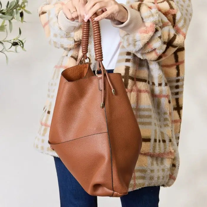 Modern brown handbag with coiled handle held by woman in plaid coat