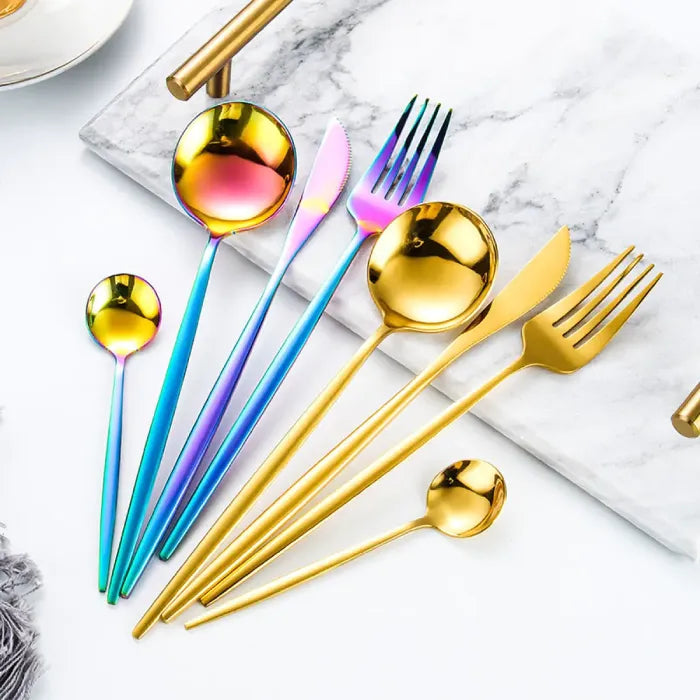 Modern gold and rainbow flatware displayed on marble surface showing various utensil styles