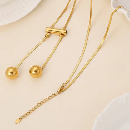 Gold snake chain necklace with cylindrical slider and two hanging spherical pendants on adjustable chains