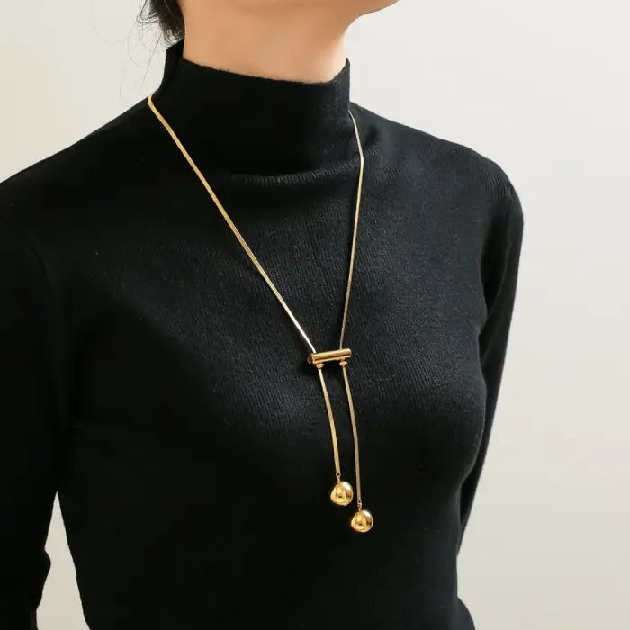 Gold pendant necklace with dual spheres styled on black turtleneck showing contemporary minimalist design