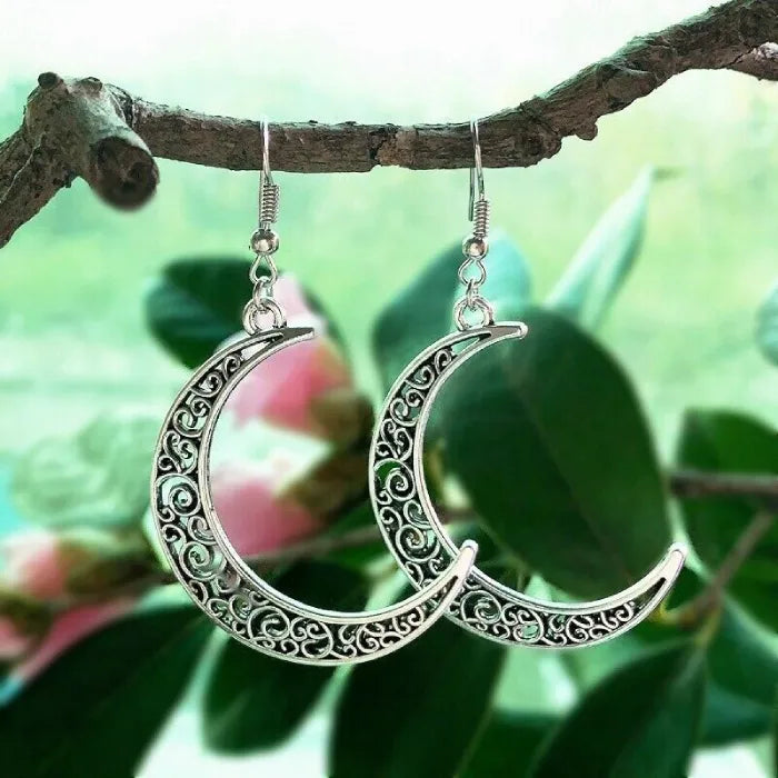 Silver crescent moon earrings with intricate patterns photographed with a green nature background.