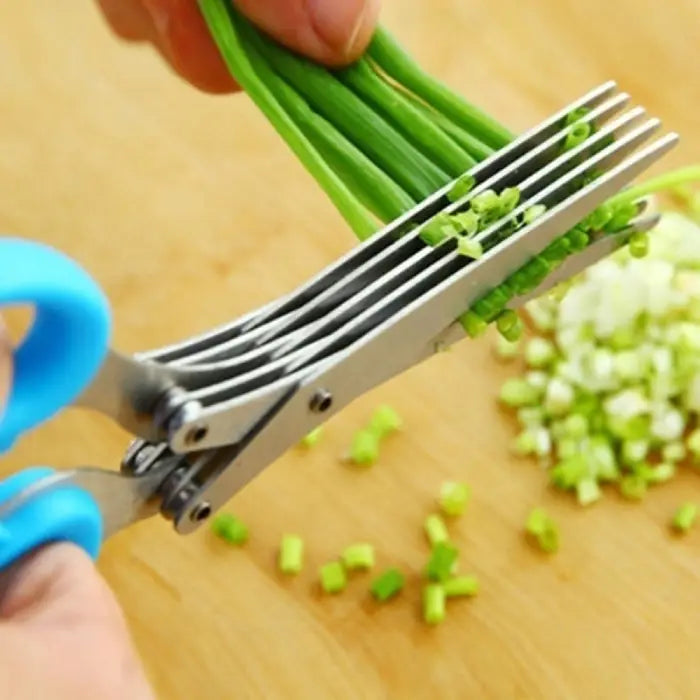 Blue-handled herb scissors chopping green onions into small pieces on a wooden cutting board.