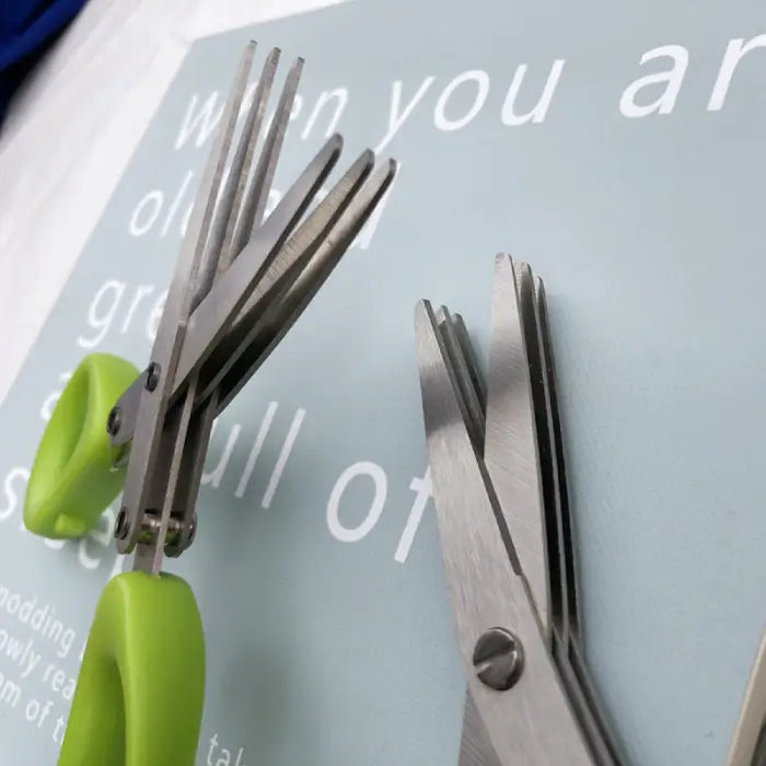 Close-up view of multi-blade herb scissors with green handle on a light background.