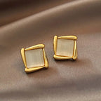 Natural white opal cat's eye earrings with gold square frames shown on satin backdrop, creating a soft luminous modern look