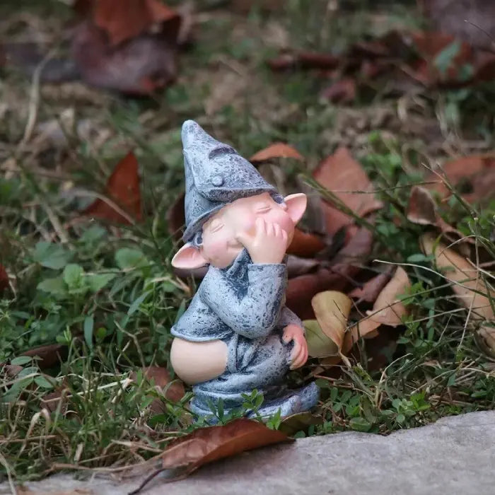 Naughty garden gnome figurine outdoors among autumn leaves, crouching with playful expression.