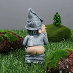 Back view of naughty garden gnome on artificial grass, showing butt and whimsical finger gesture.