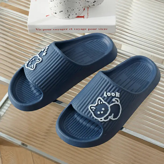 : Navy blue bathroom slides featuring white cartoon cat design on textured base against striped surface