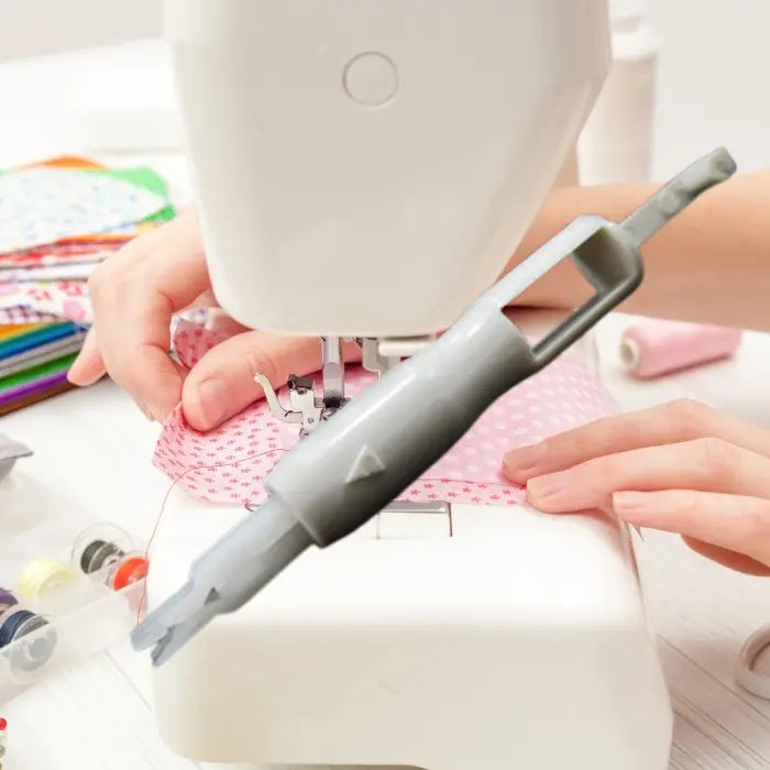 Needle threader in action on a sewing machine with hands guiding pink polka-dot fabric.