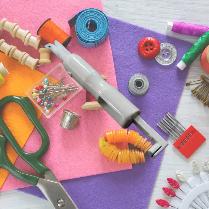 Needle threader on top of colorful felt sheets with pins, scissors, and sewing notions.
