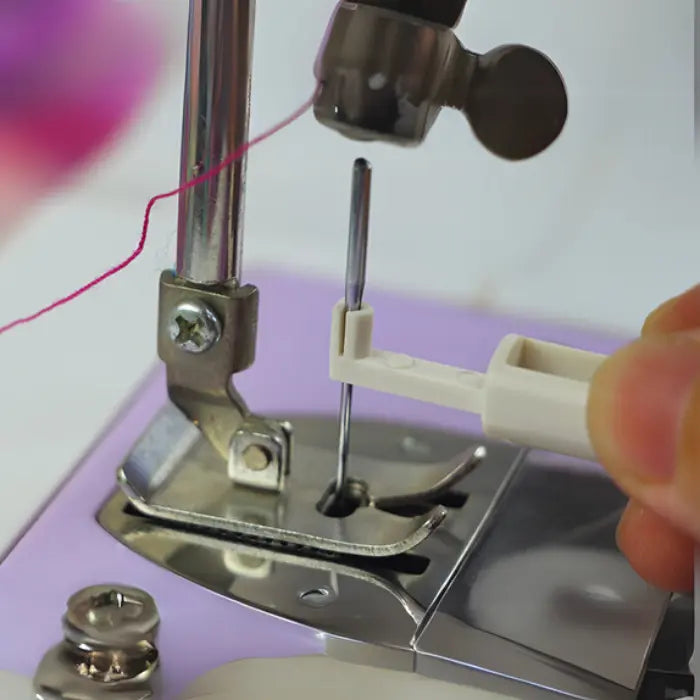 Needle threader being used to guide thread through machine needle with purple accents.