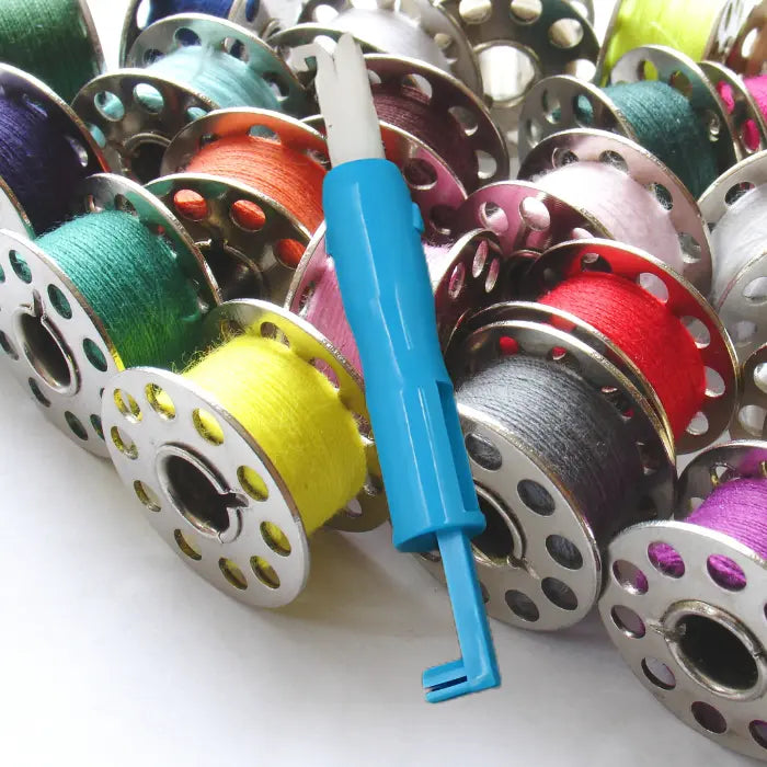Needle threader placed over a vibrant mix of multicolor thread bobbins for sewing.