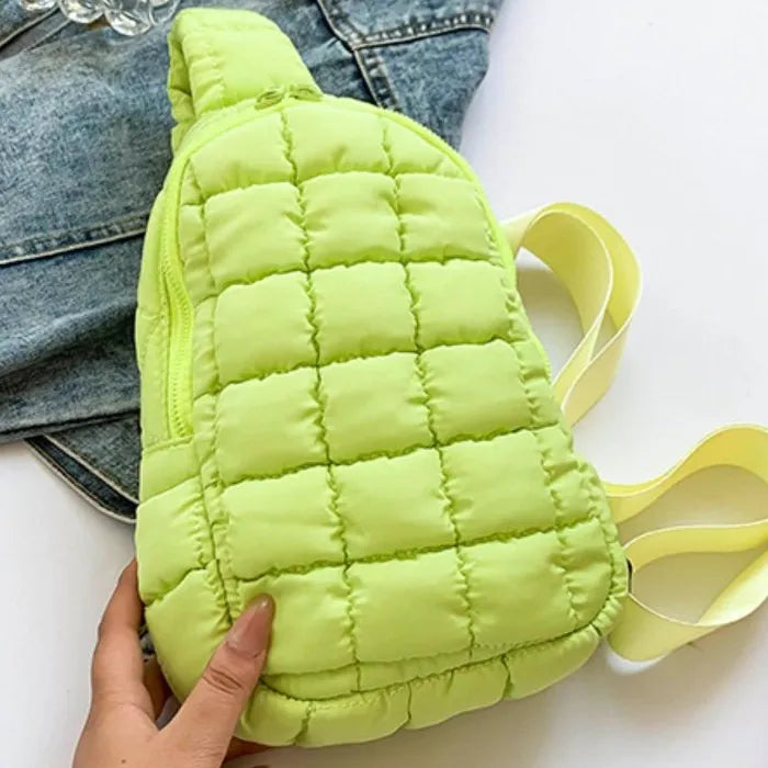 Neon yellow puffer sling bag with quilted design, zipper closure and adjustable strap, displayed on denim jacket background