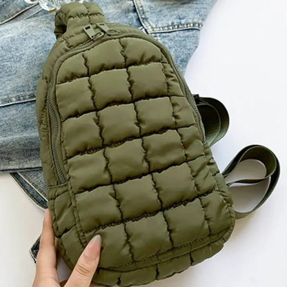 Olive green quilted sling bag with zipper closure and adjustable strap, displayed on denim jacket background