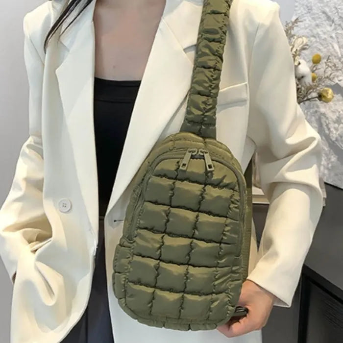 Olive green quilted sling bag worn over cream blazer, black top underneath, partial view of person's torso and hand