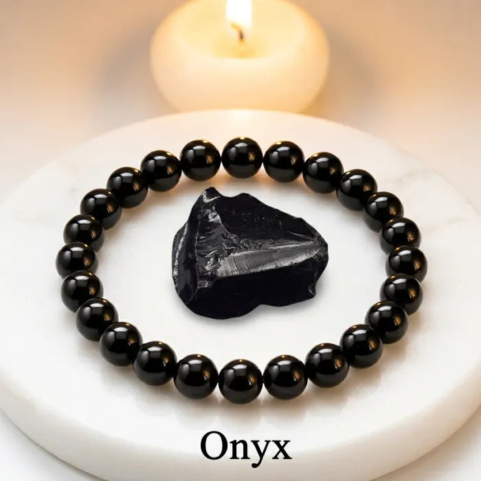 Onyx Bracelet with black beads and raw stone on white surface with candle glow, calming healing crystal jewelry for stress relief