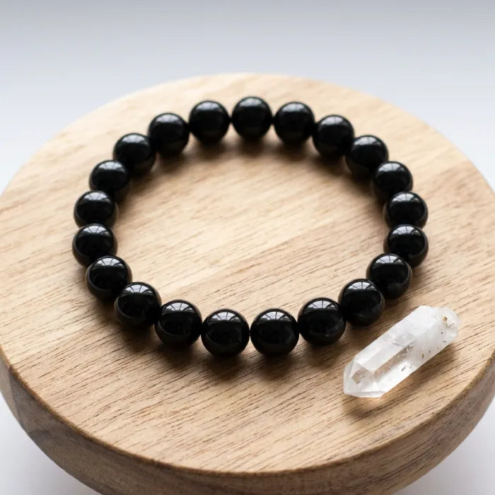 Onyx Bracelet with glossy black beads on wooden platform, minimalist crystal jewelry design promoting balance and calm energy daily