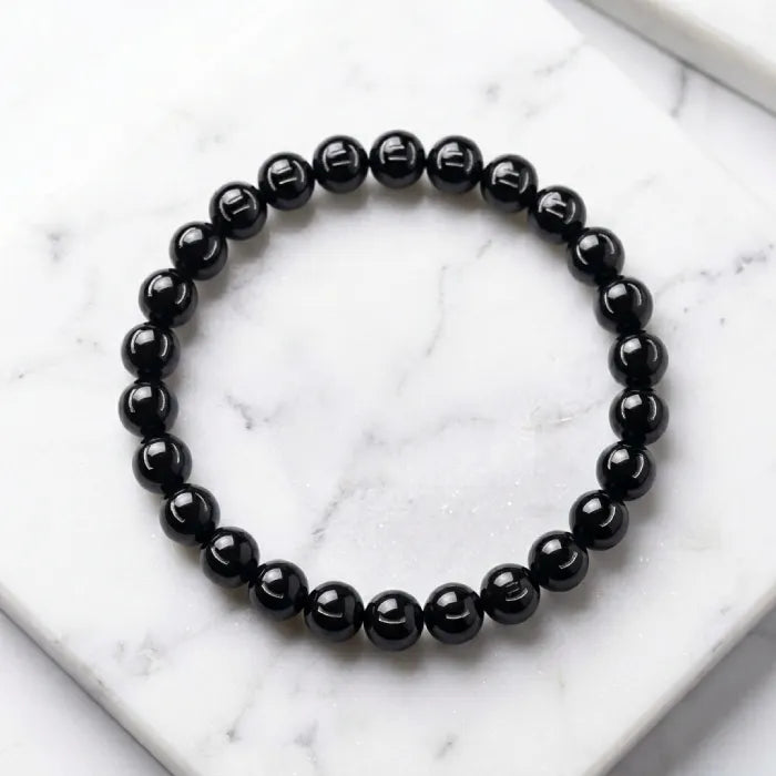 Onyx Bracelet with smooth black beads on marble background, modern minimalist crystal jewelry supporting calm and focus daily